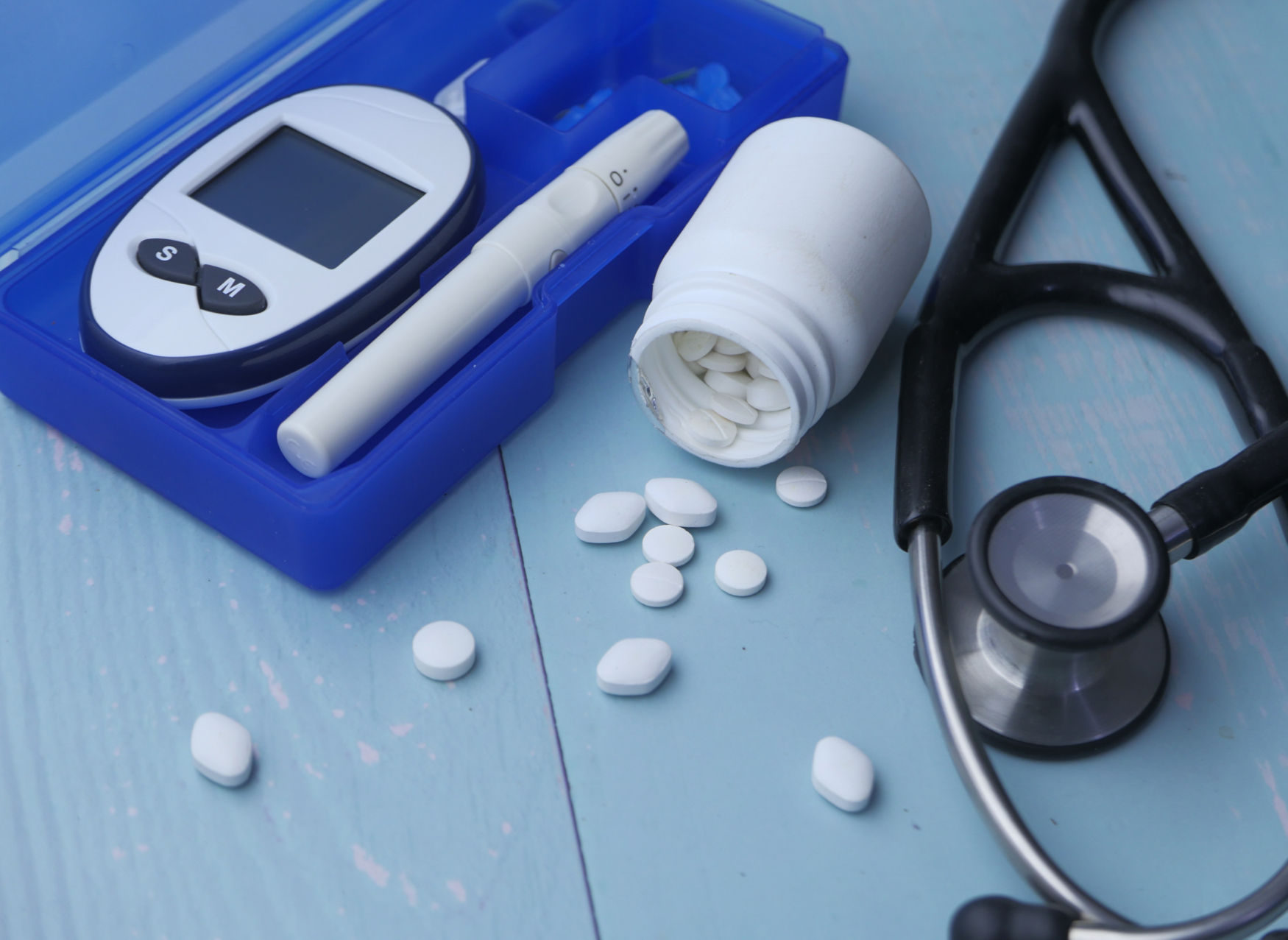 An open bottle of pills, a stethoscope, and a blood glucose meter sit next to each other on a tabletop